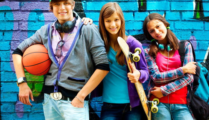 Foto: Drei Jugendliche mit Skateboard lehnen an einer Ziegelwand.